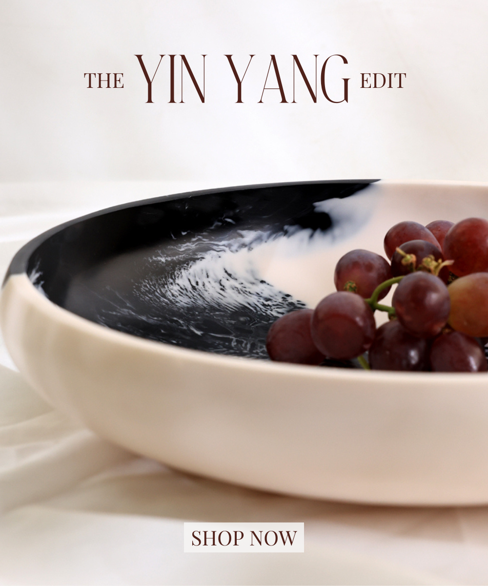Bowl with black interior and white exterior containing grapes, branded 'The Yin Yang Edit'.