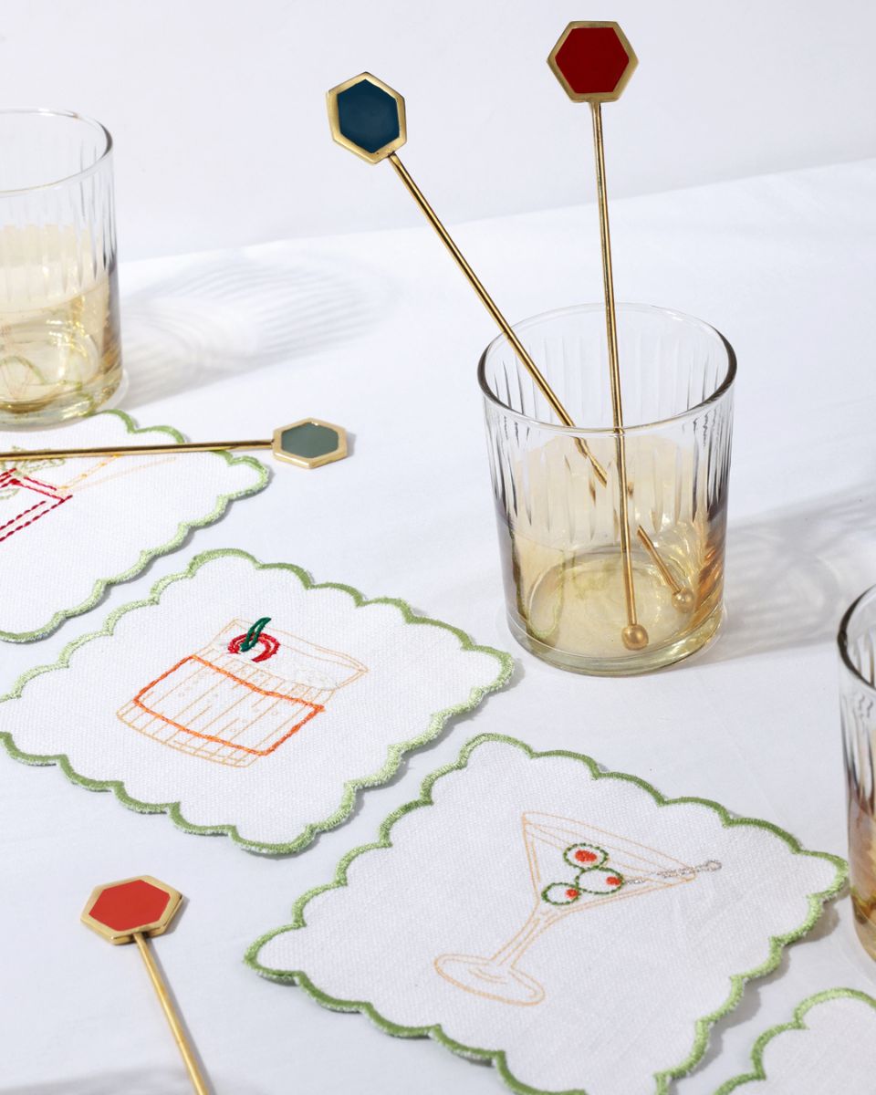 Decorative cocktail stirrers with hexagonal ends on a glass of drink, surrounded by embroidered coasters.